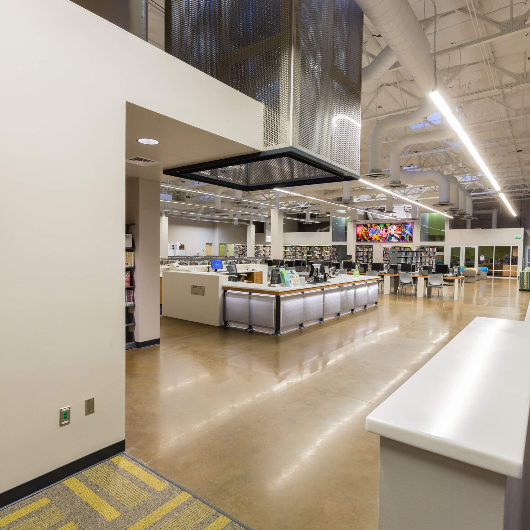 Modern library interior with polished floors, a central information desk, bookshelves in the background, and bright overhead lighting