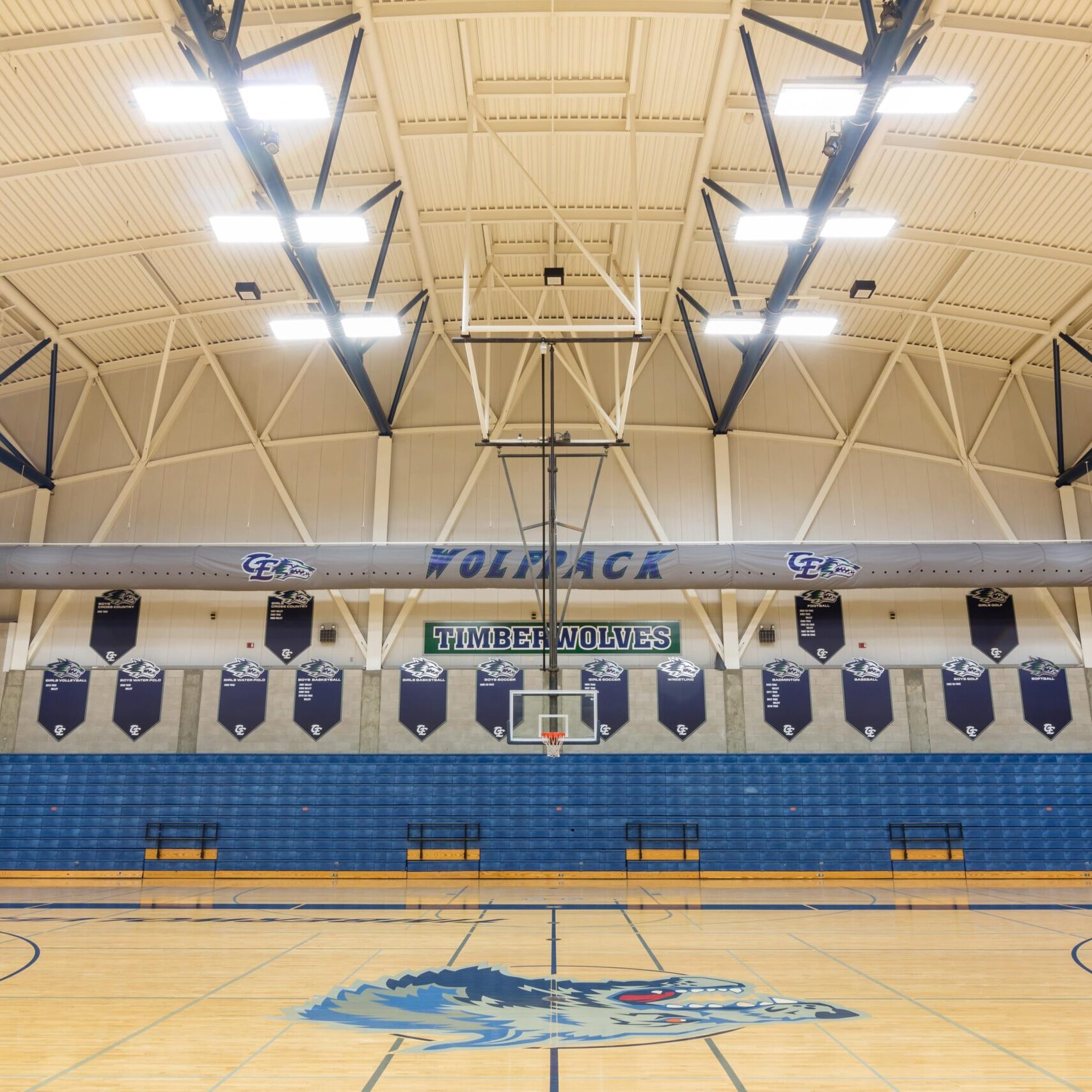 Clovis east high school gymnasium interior shot with the wolves logo in the center and lights on showing the scale of the building and cleanliness with blue bleachers and upper racks