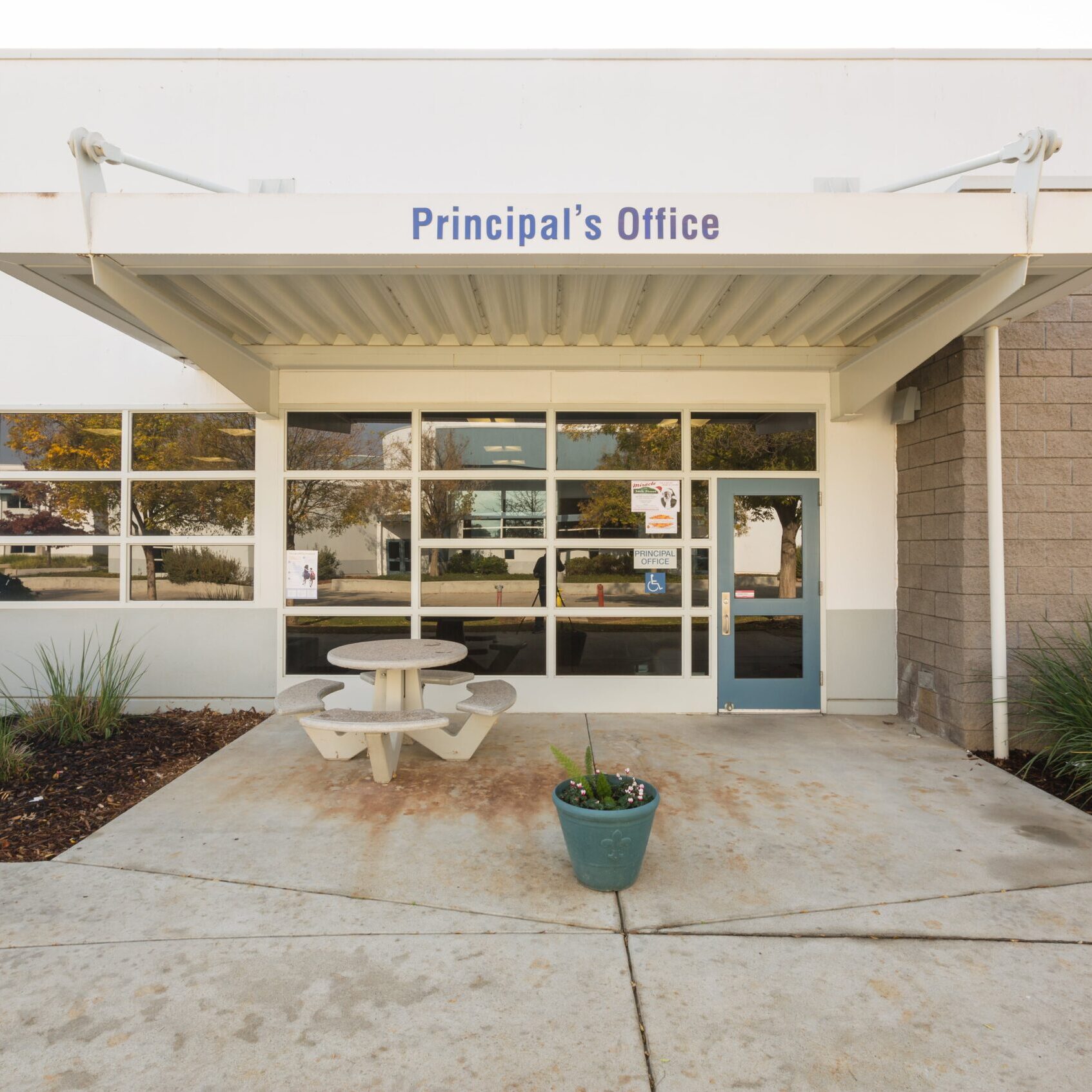 exterior of the principals office for clovis east high school during the daytime with a small lunch table and bushes laid out before the entrance