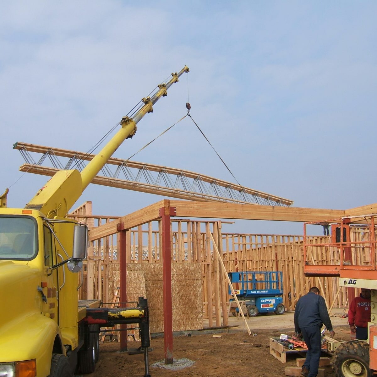 A construction site photo of a Hindu temple. A large yellow crane is lifting a wooden roof truss into place over the framed walls of the building. There are workers and other construction vehicles nearby. The date "FEB 2 2007" is visible in the bottom right corner.