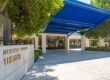 exterior view of the mercedes edwards theatre for clark intermediate school with blue ceiling cover and lush trees before the entrance in the daytime