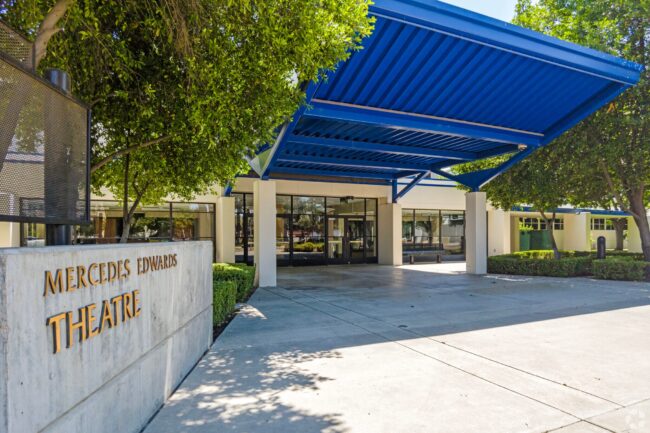 exterior view of the mercedes edwards theatre for clark intermediate school with blue ceiling cover and lush trees before the entrance in the daytime