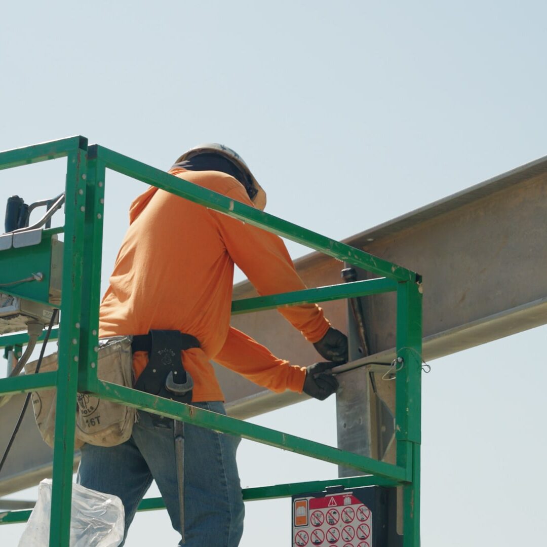 man in construction shirt on a forklift installing beams on a sunny afternoon