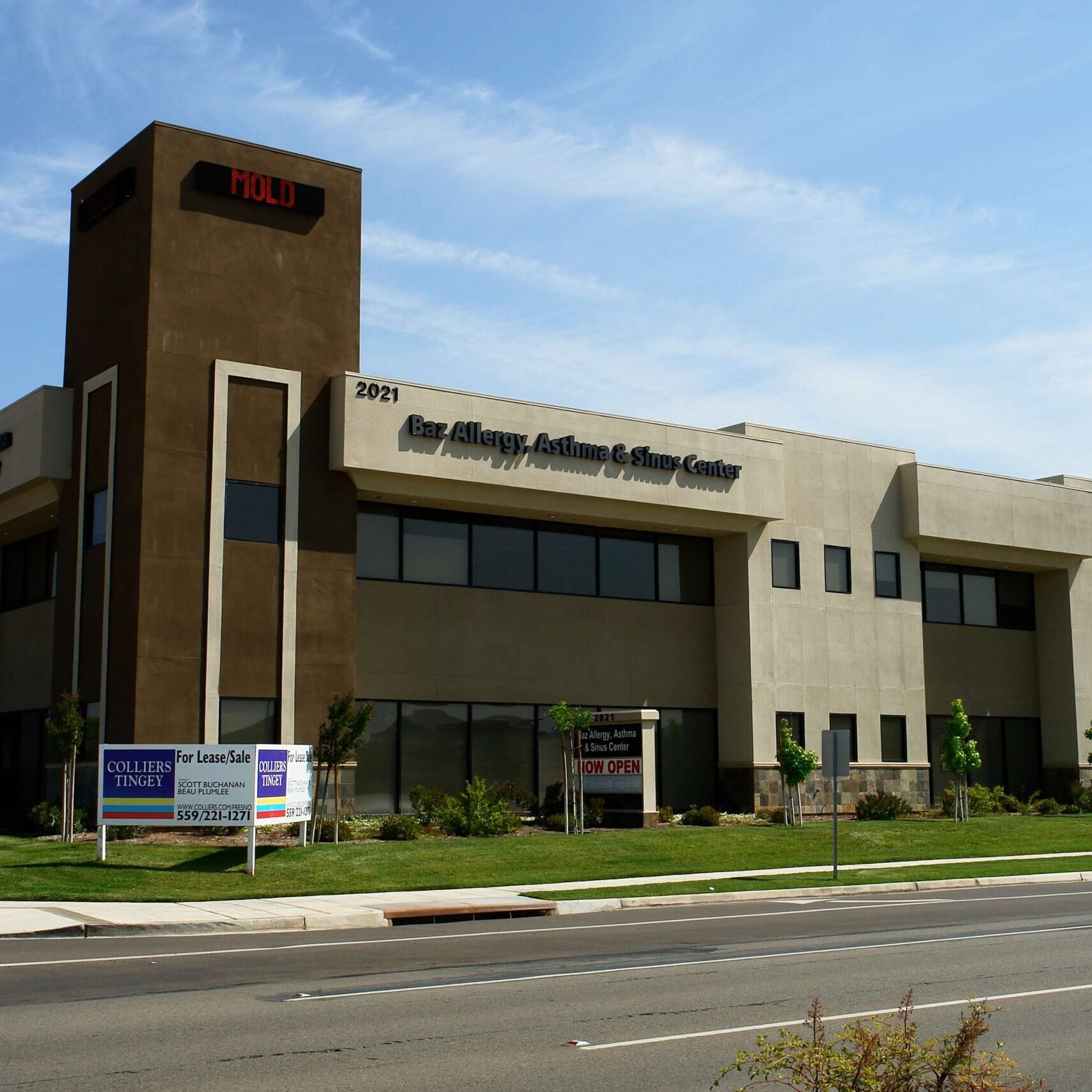 A modern, two-story building in Clovis, California, with a prominent sign for "Baz Allergy, Asthma, & Sinus Center." The building is beige with a tall brown tower on the left side. A "For Lease" sign is visible in the foreground.
