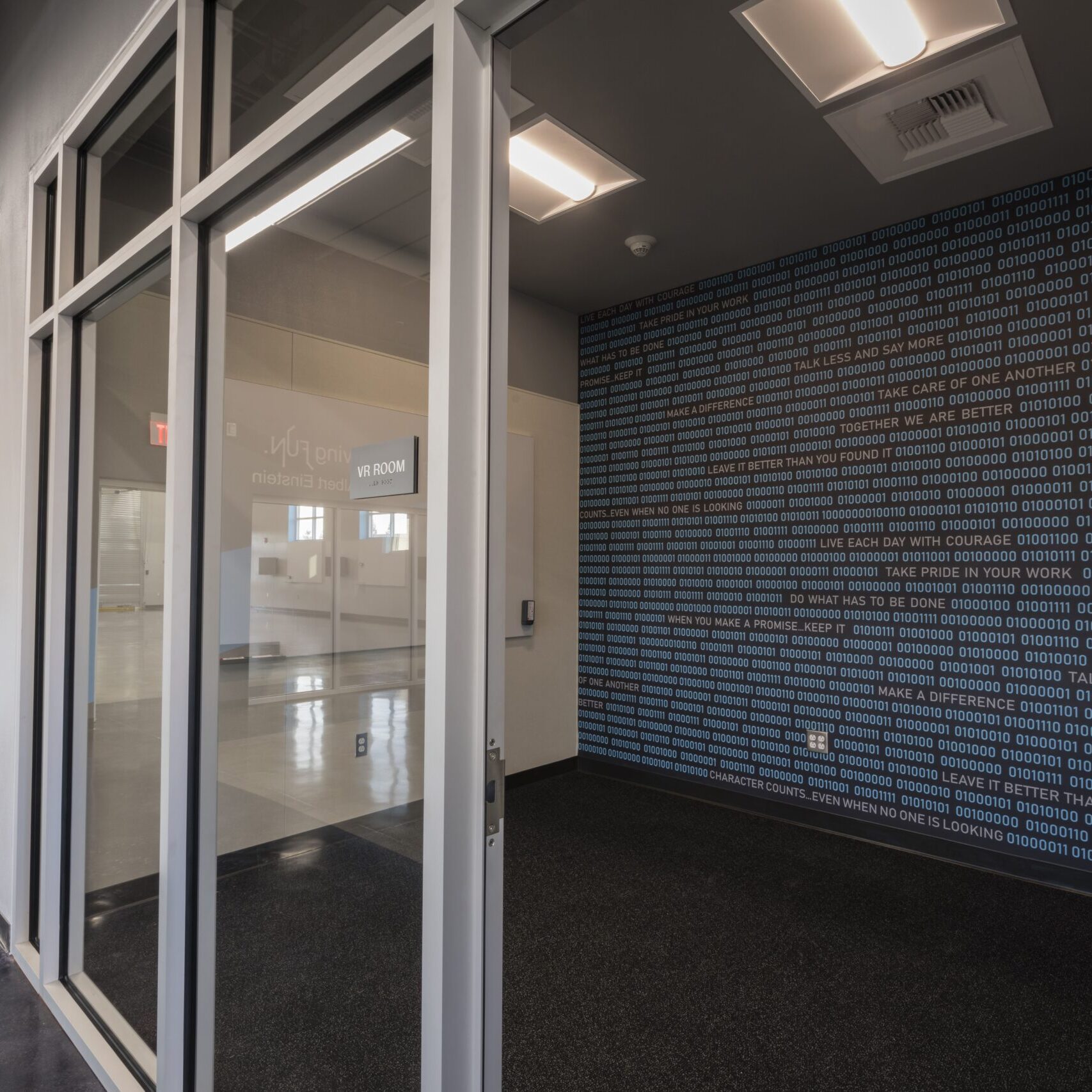 A shot of a building's interior hallway with a blue-painted wall and a large glass-paneled wall. A mural on the wall opposite the glass wall features binary code and text.