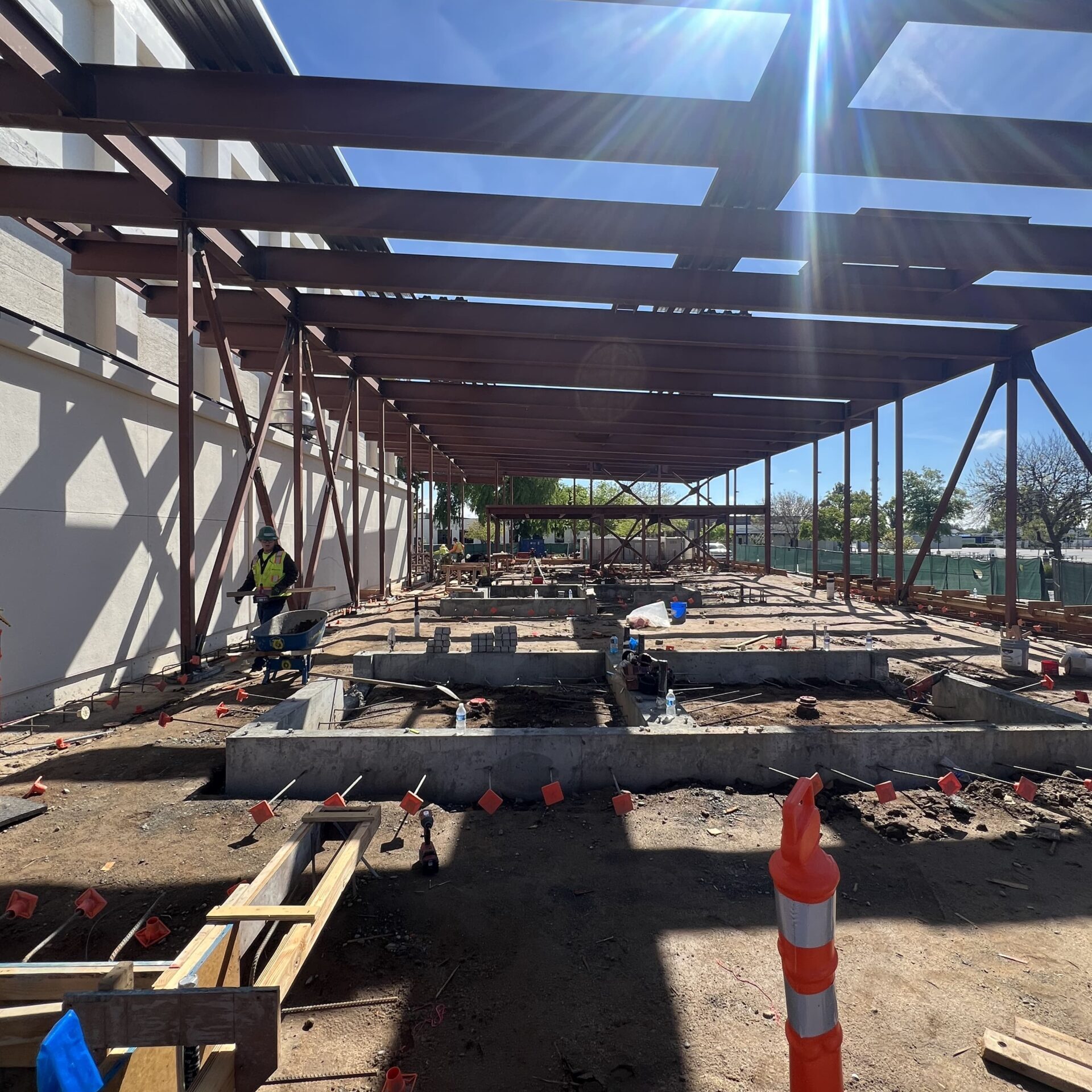 An image of a building's interior from a low angle. Sunlight streams in from the side. The steel frame of the roof and ceiling is visible, and the ground floor has concrete forms and exposed pipes.