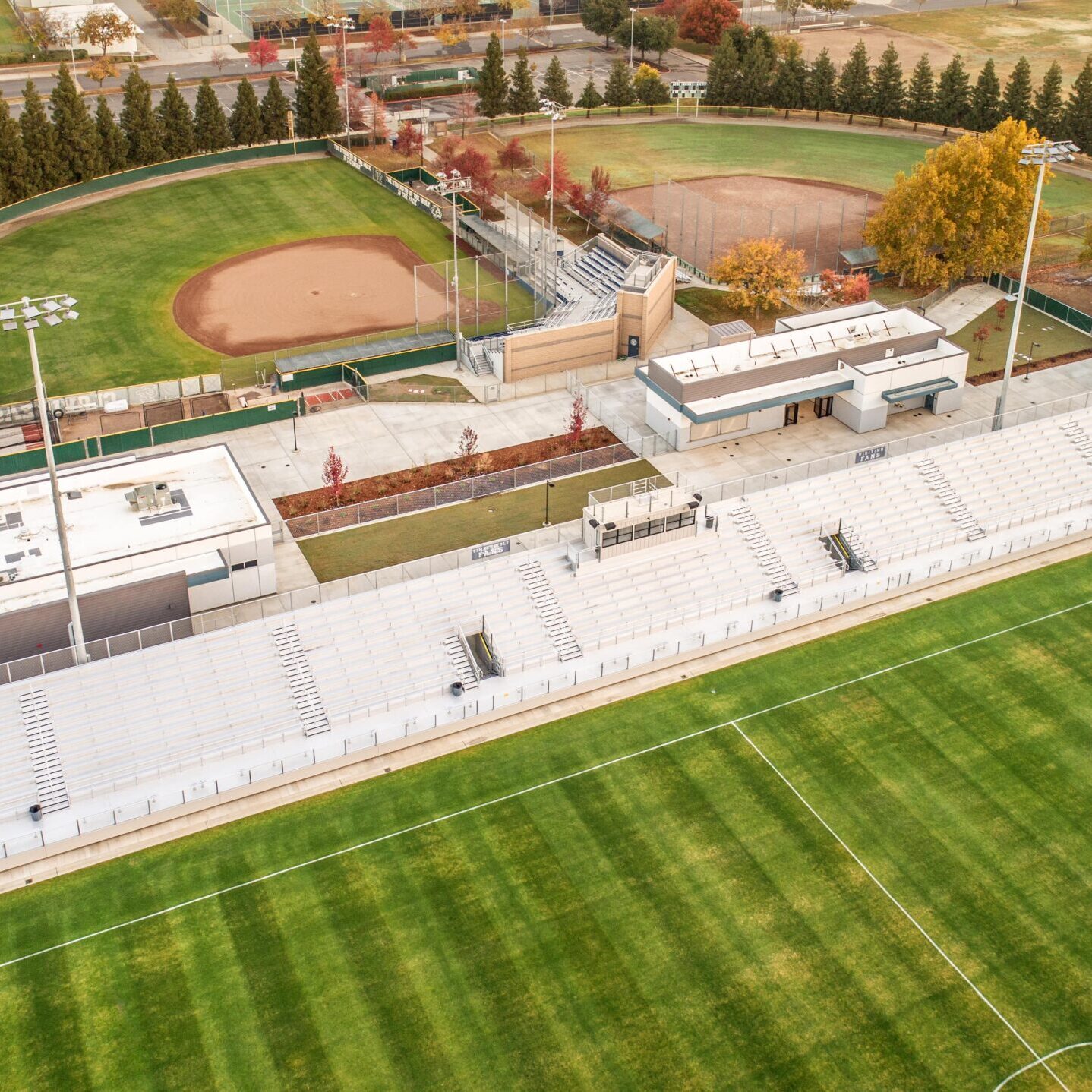An aerial view of the stadium complex, showing the soccer field, bleachers, and a nearby baseball diamond with a running track.