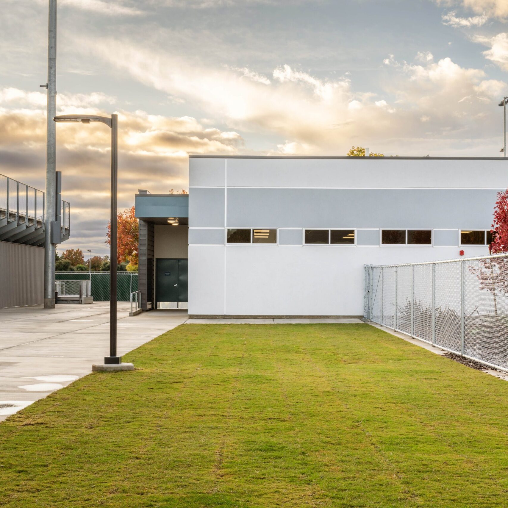 A ground-level shot of a building next to the stadium, showing a chain-link fence and a small patch of grass.