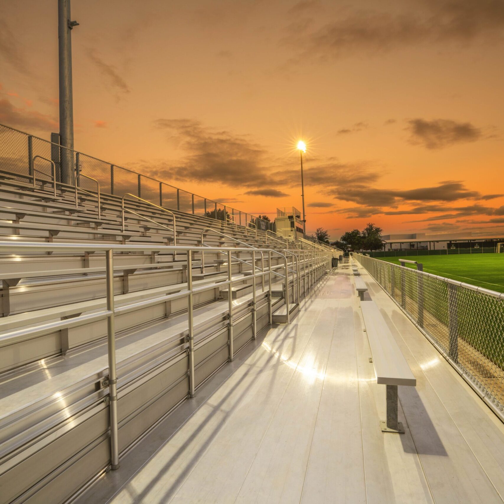 A ground-level shot from the top of the bleachers at sunset, showing the walkway and a bench.