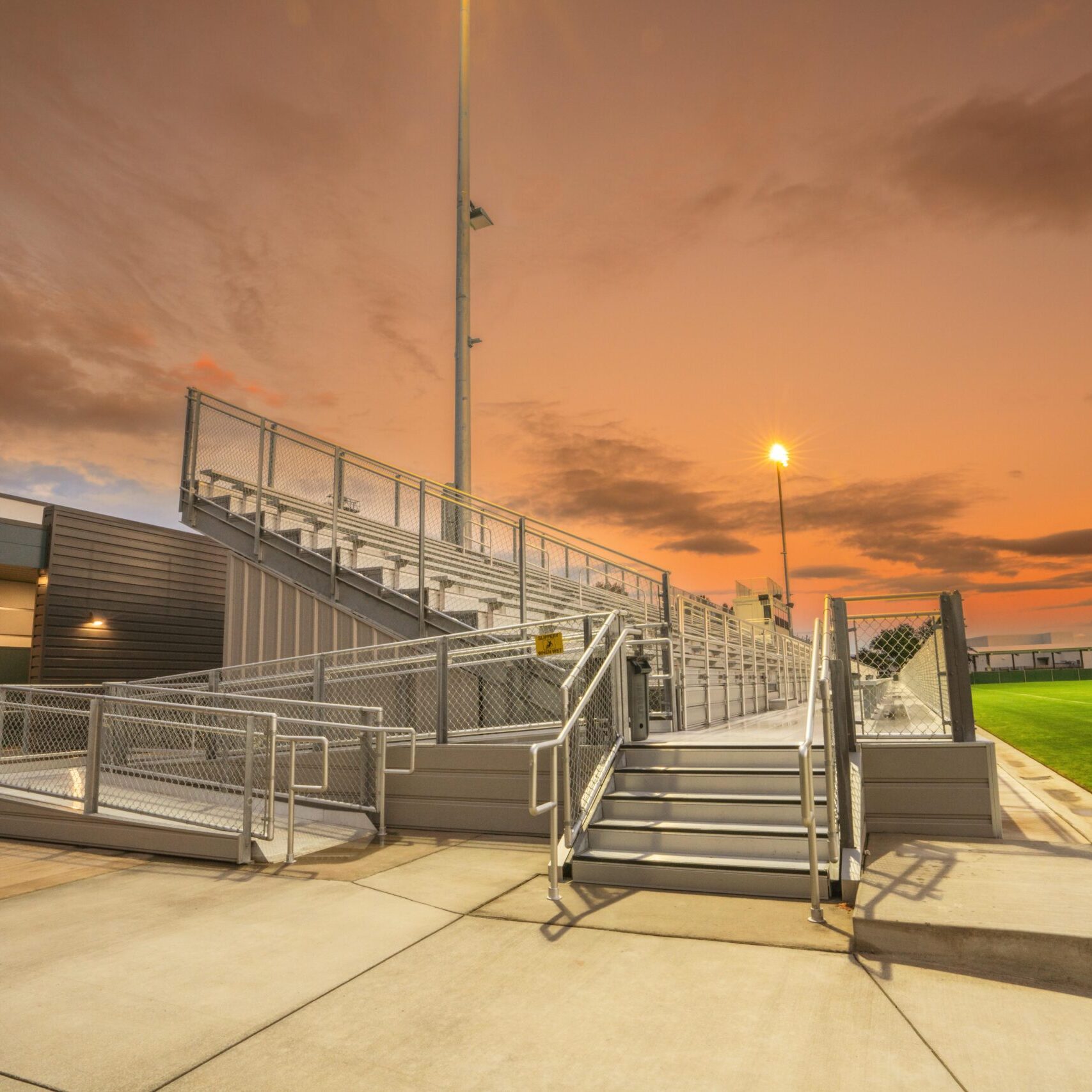 A ground-level shot of the stadium entrance, with stairs and a ramp leading to the bleachers at sunset.