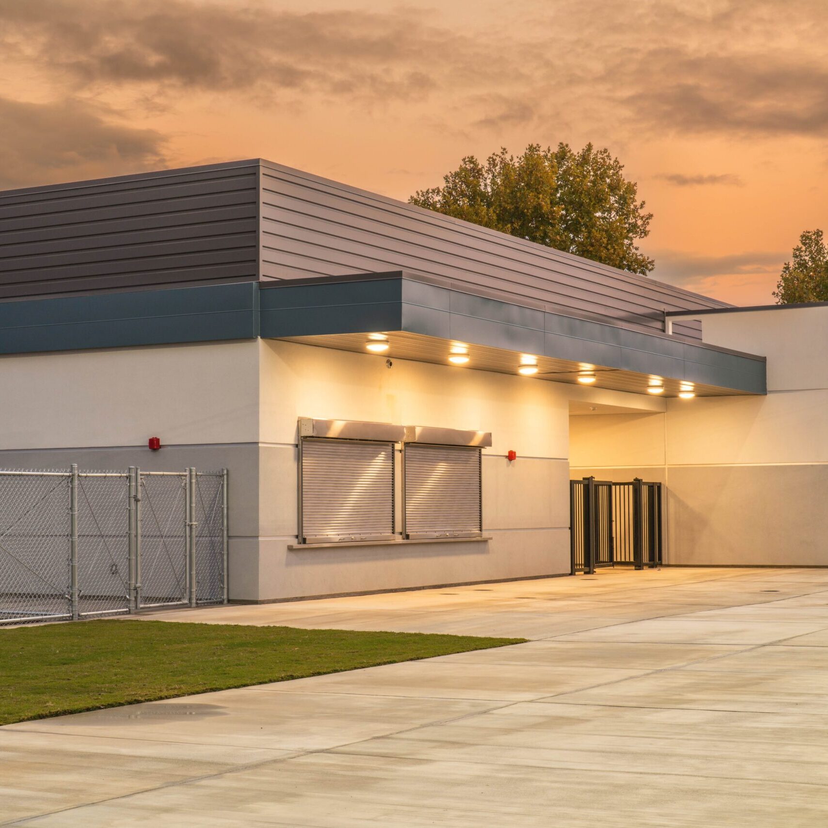 A ground-level shot of a building with roll-down windows and an entrance with turnstiles, under a sky with sunset colors.