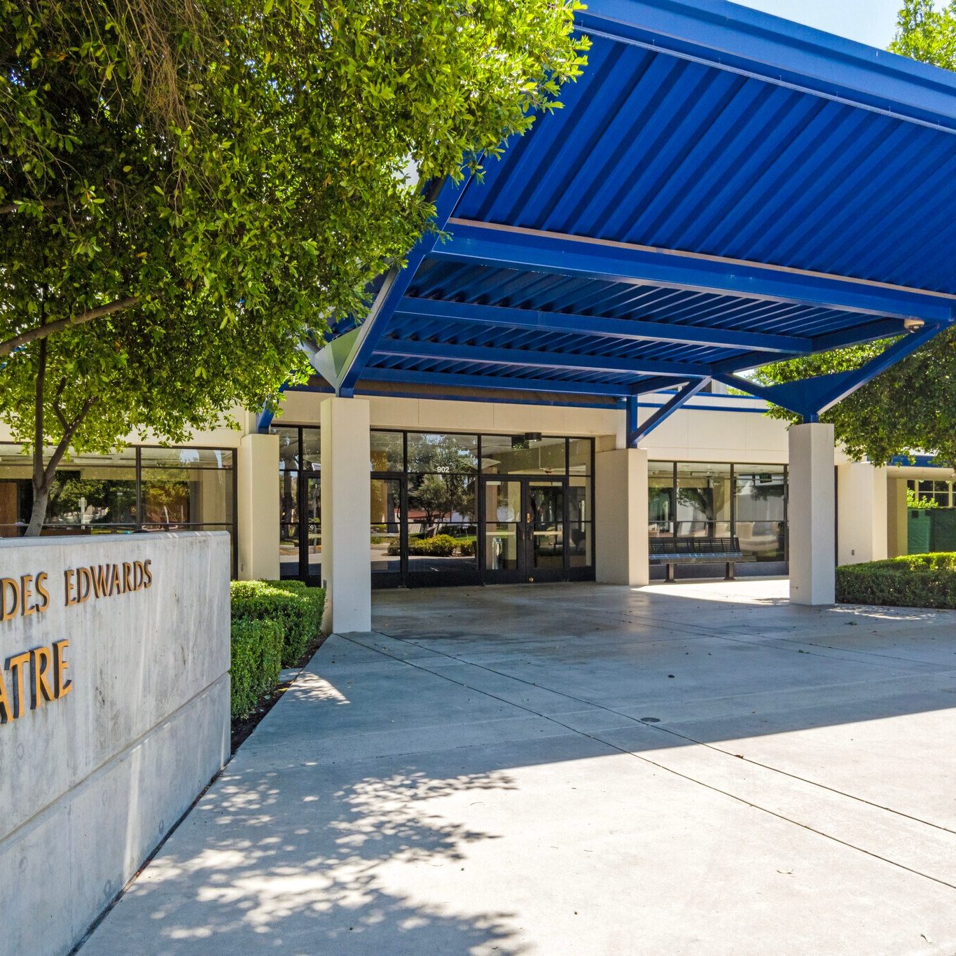 exterior view of the mercedes edwards theatre for clark intermediate school with blue ceiling cover and lush trees before the entrance in the daytime