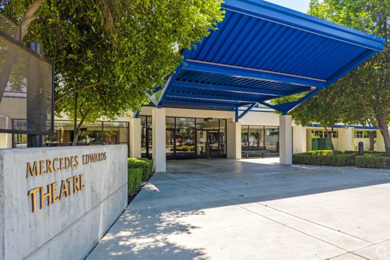 exterior view of the mercedes edwards theatre for clark intermediate school with blue ceiling cover and lush trees before the entrance in the daytime